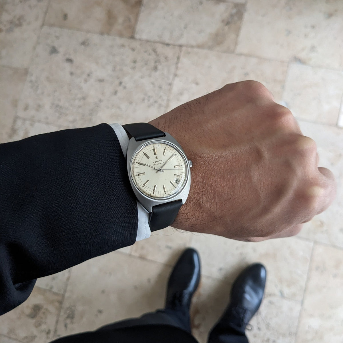 Zenith Automatic reference GR 720001 worn on a wrist over a dark sleeve, with tiled flooring and shoes visible below.