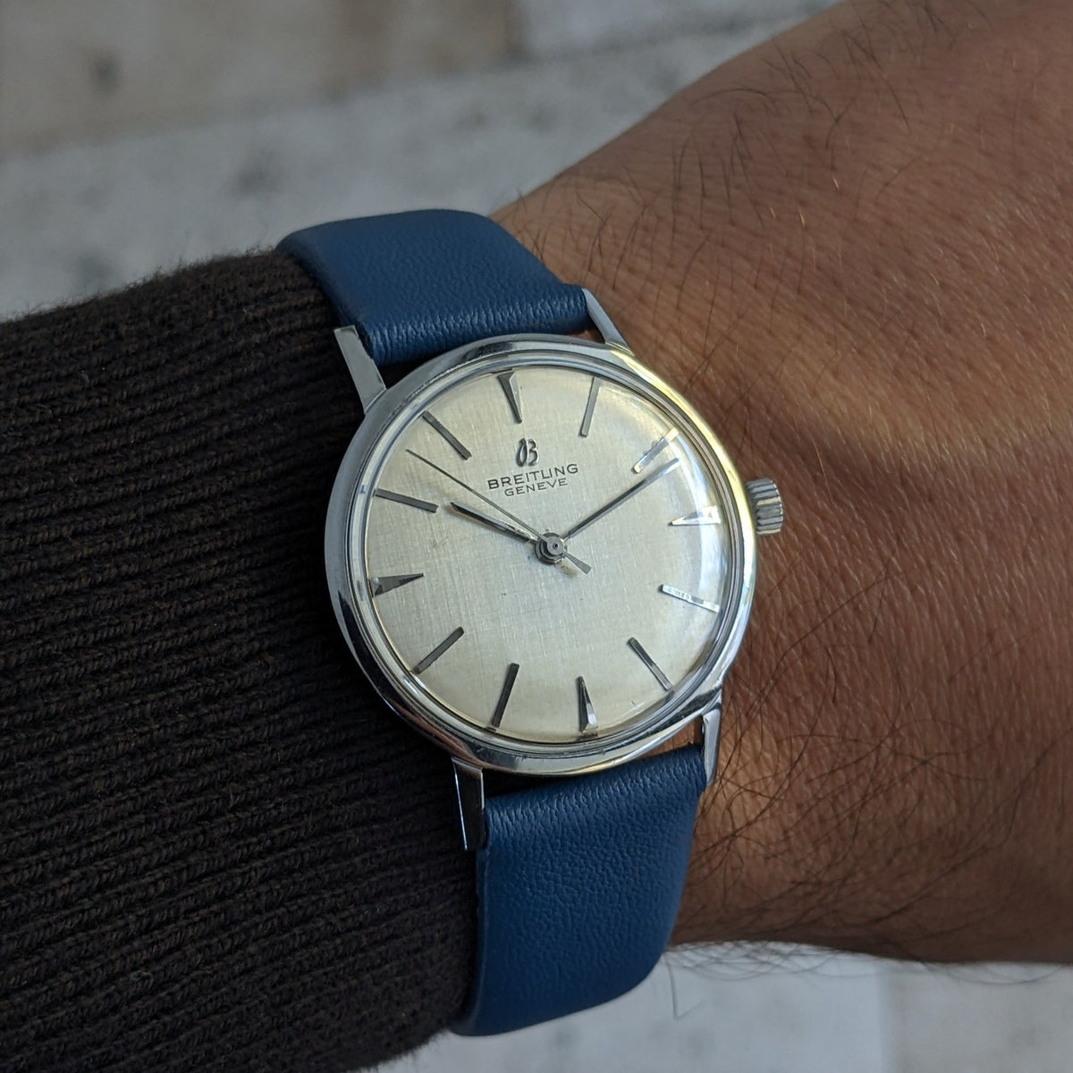 Breitling Automatic watch worn on a wrist, showing the cream dial, slim polished case and blue strap against a dark sleeve.