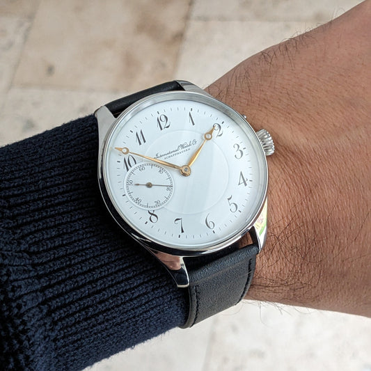 IWC Schaffhausen कलाई घड़ी पहने हुए, सफेद अंक, सुनहरे हाथ, छोटे सेकंड्स डायल और काले चमड़े की पट्टी के साथ।