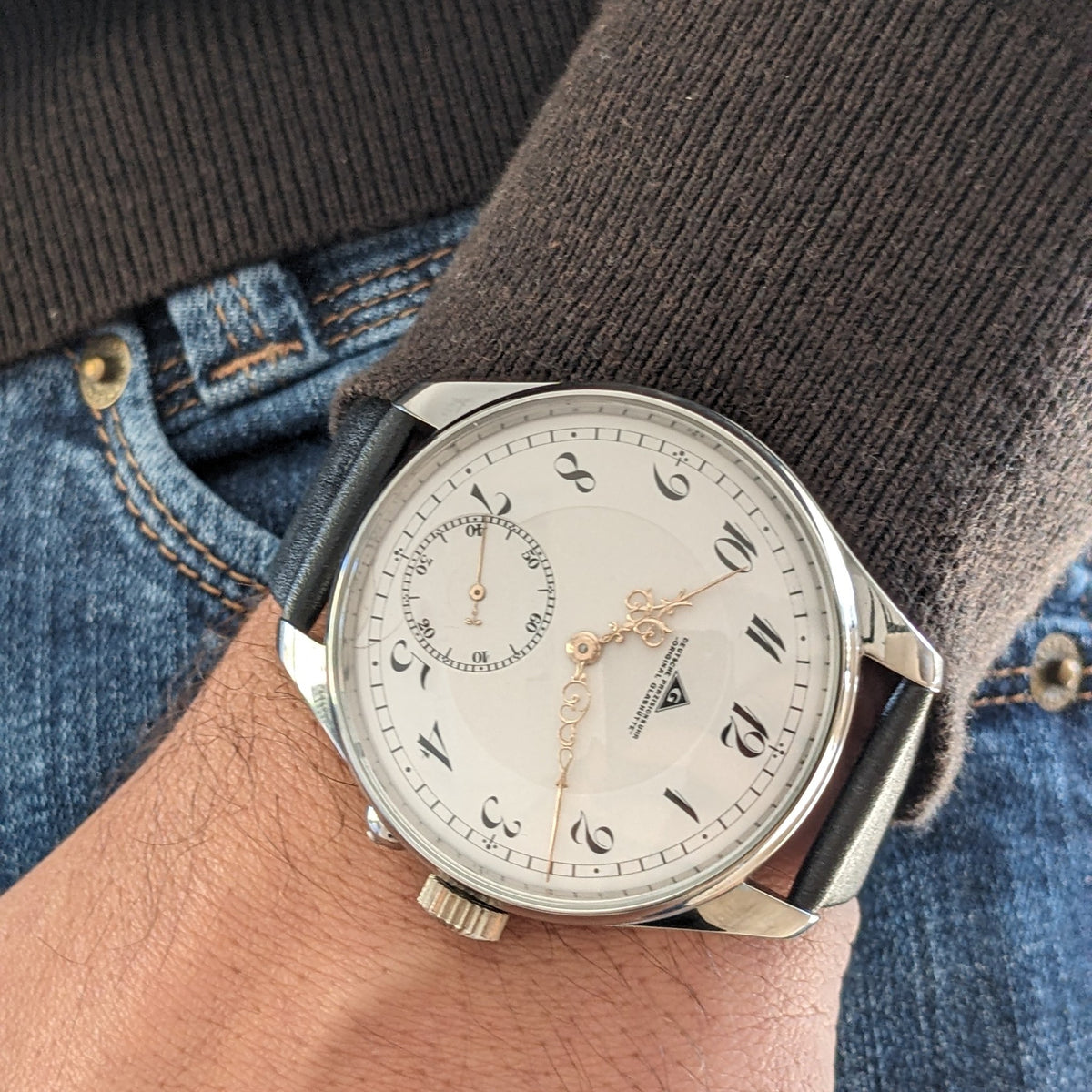 Deutsche Präzisionsuhr „Original Glashütte” am Handgelenk über Denim und einem dunklen Pullover, mit weißem Zifferblatt und s