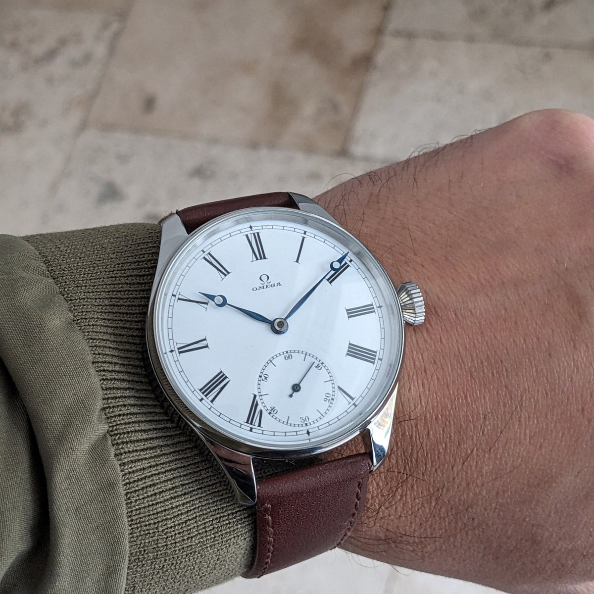 Orologio Omega indossato al polso, con quadrante bianco a numeri romani, lancette blu, sub-quadrante dei secondi e cinturino in pelle marrone.