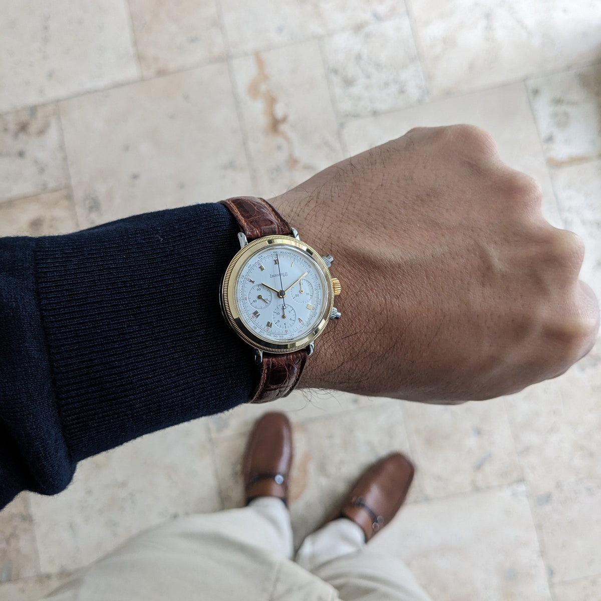 Eberhard & Co.. Godron Chrono reference 32031 is shown on a wrist above a tiled floor, paired with a dark sleeve and brown shoes.