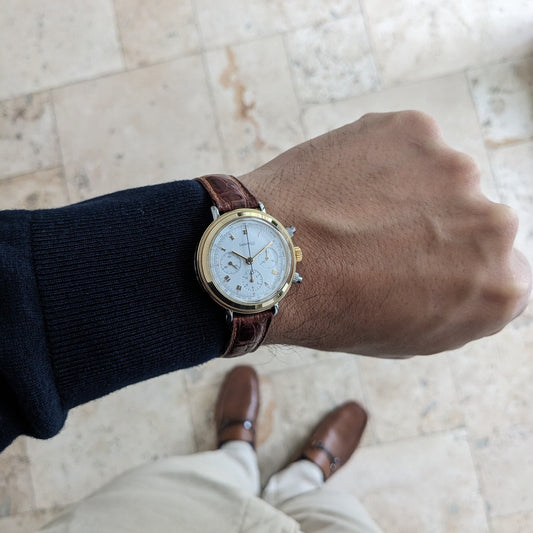 Eberhard & Co. Godron Chrono Referenz 32031 am Handgelenk über einem gefliesten Boden, kombiniert mit dunklem Ärmel und braunen Schuhen.