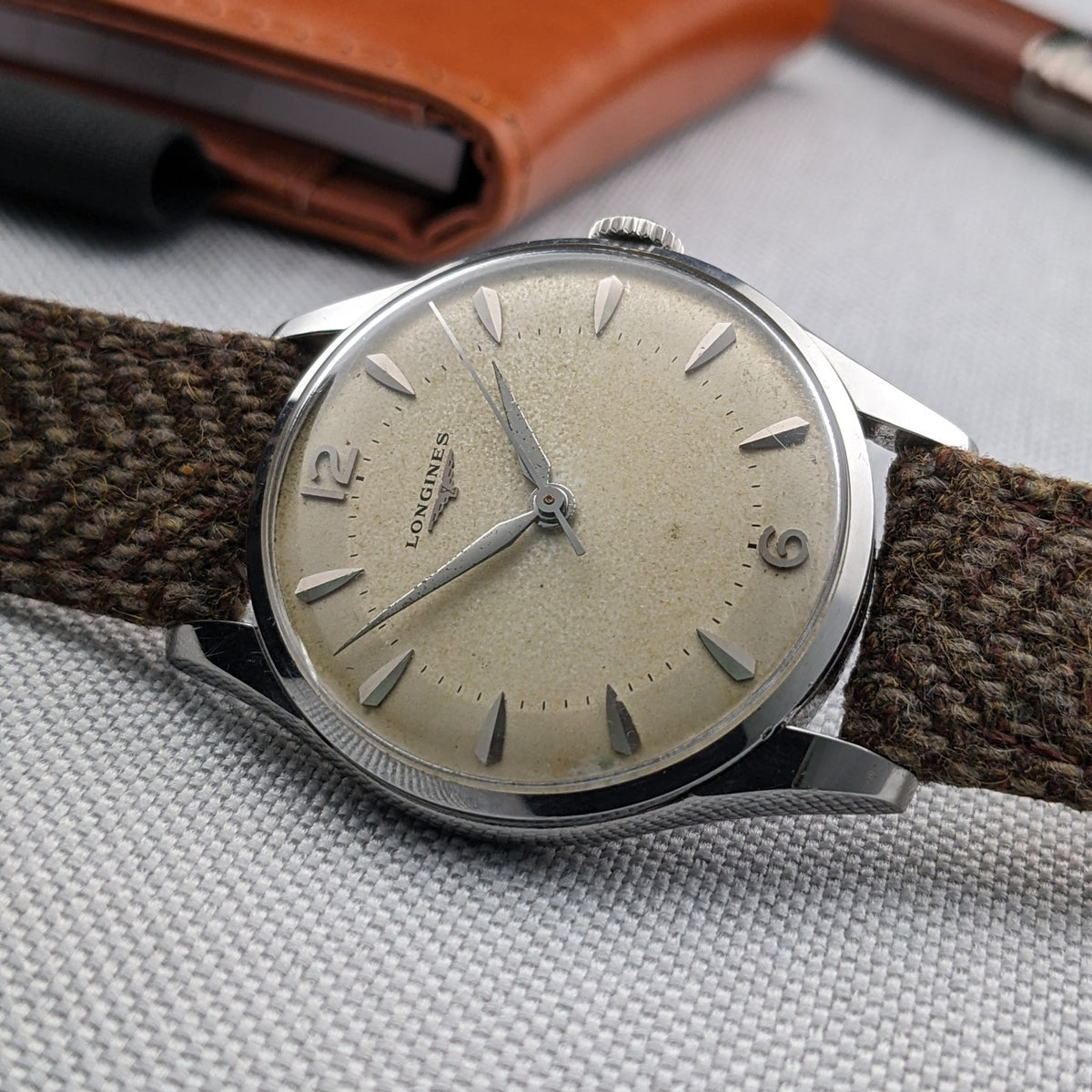 Low-angle view of the Longines Classic reference 8135-5 showing the cream dial, crown, silver case and woven strap against gray fabric.