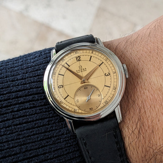 Reloj Omega Sector con esfera crema y correa negra mostrado en una muñeca contra una manga de punto oscuro.