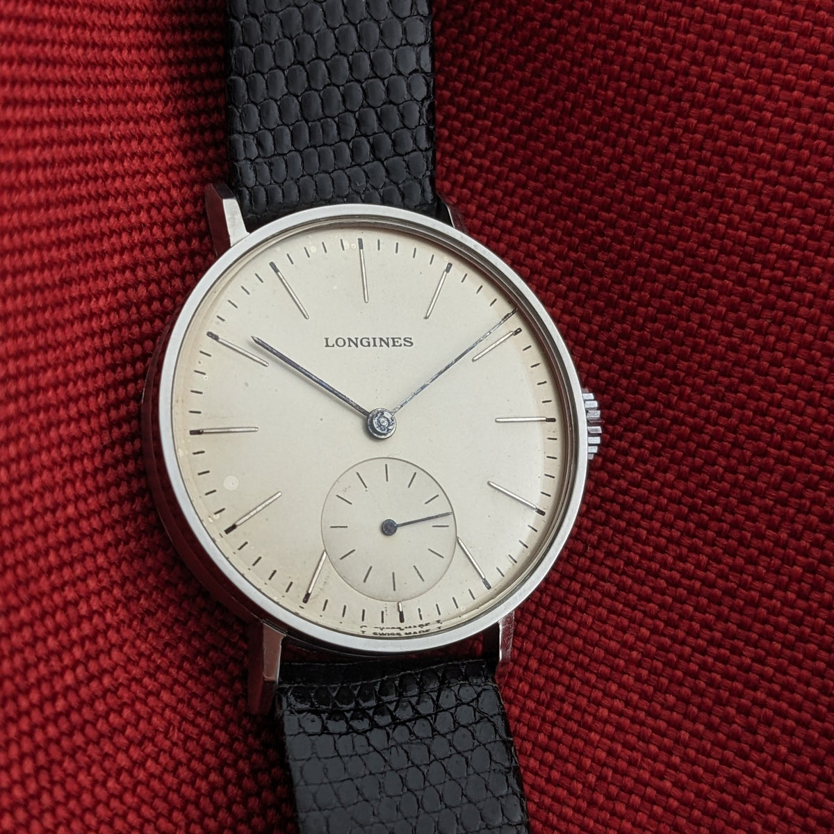 Close front view of the Longines Calatrava reference 20757 on red fabric, showing its light dial, slim hands, markers, and small seconds.