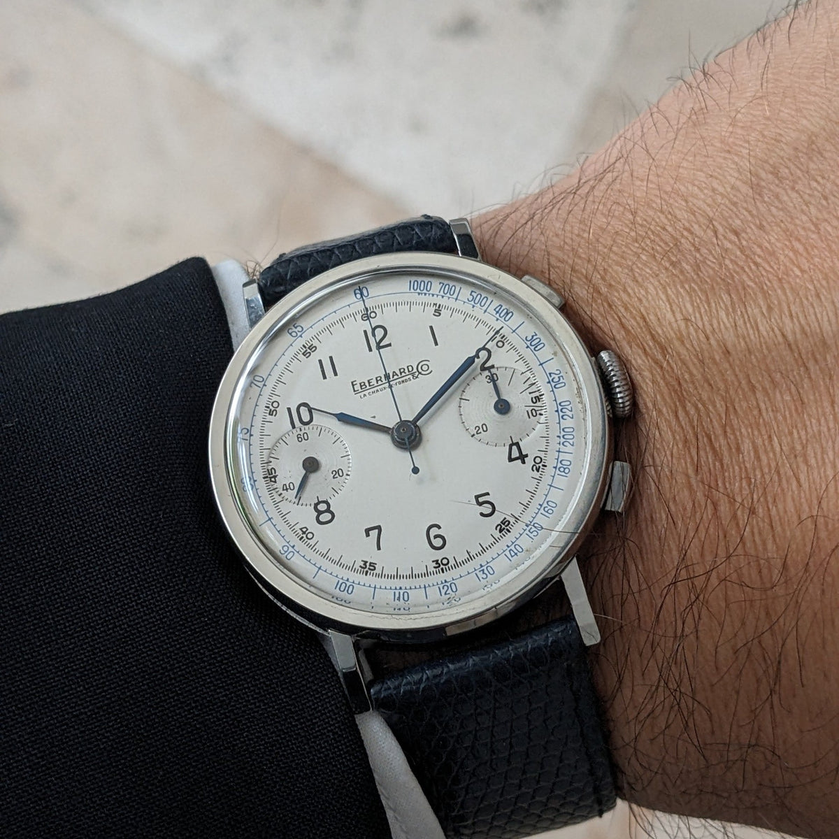 Close wrist view of the Eberhard & Co. Pre-Extra Fort showing its cream chronograph dial, blue scales, crown and dark blue strap.