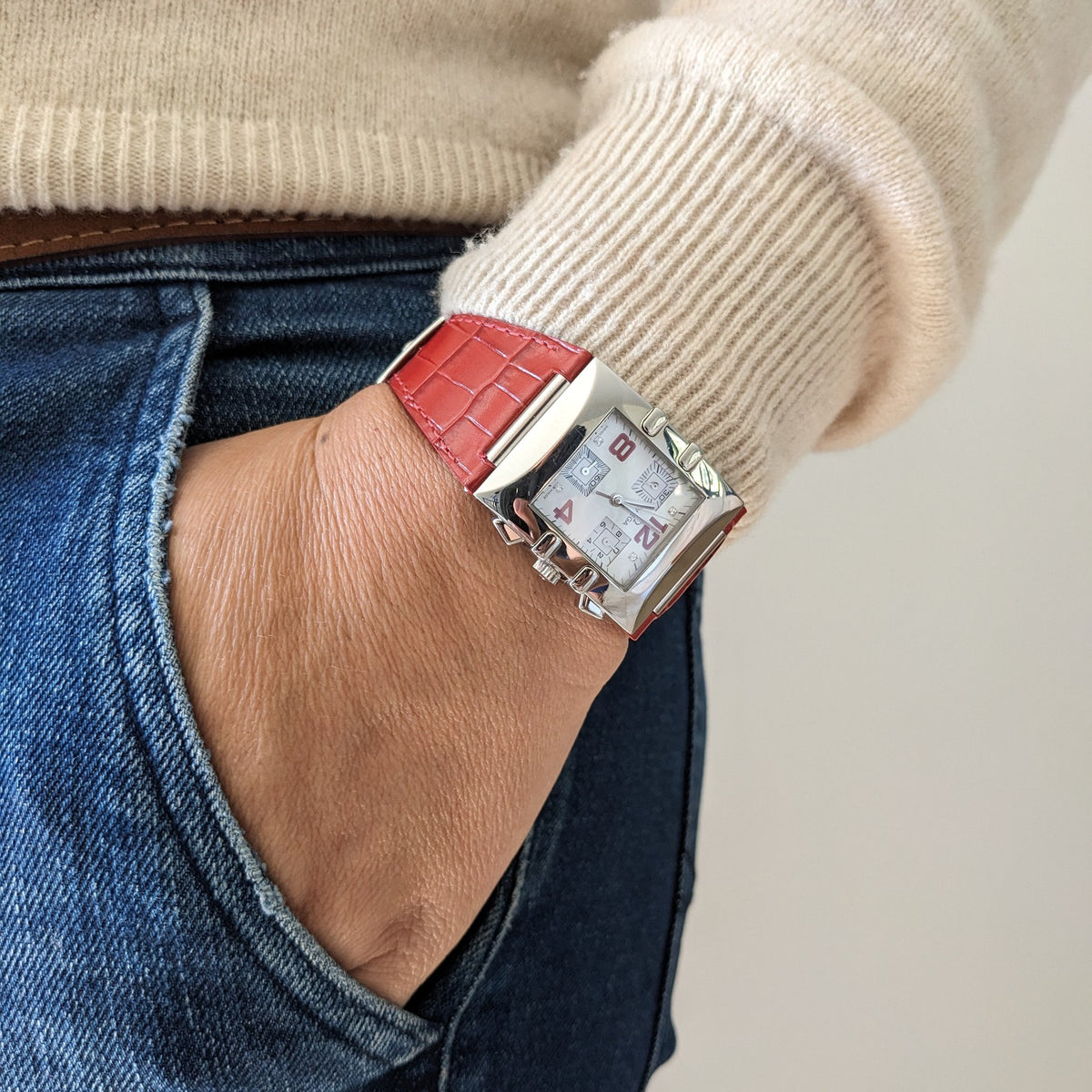 Wrist view of the Omega Constellation Quadra 1841.73.31 beneath a cream sleeve, with the red strap and white dial visible.