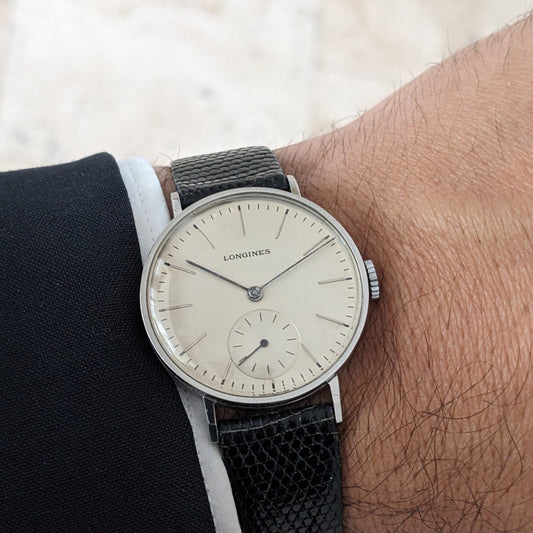 Close wrist view of the Longines Calatrava reference 20757, showing its light dial, black textured strap, and crown beside a white shirt cuff.