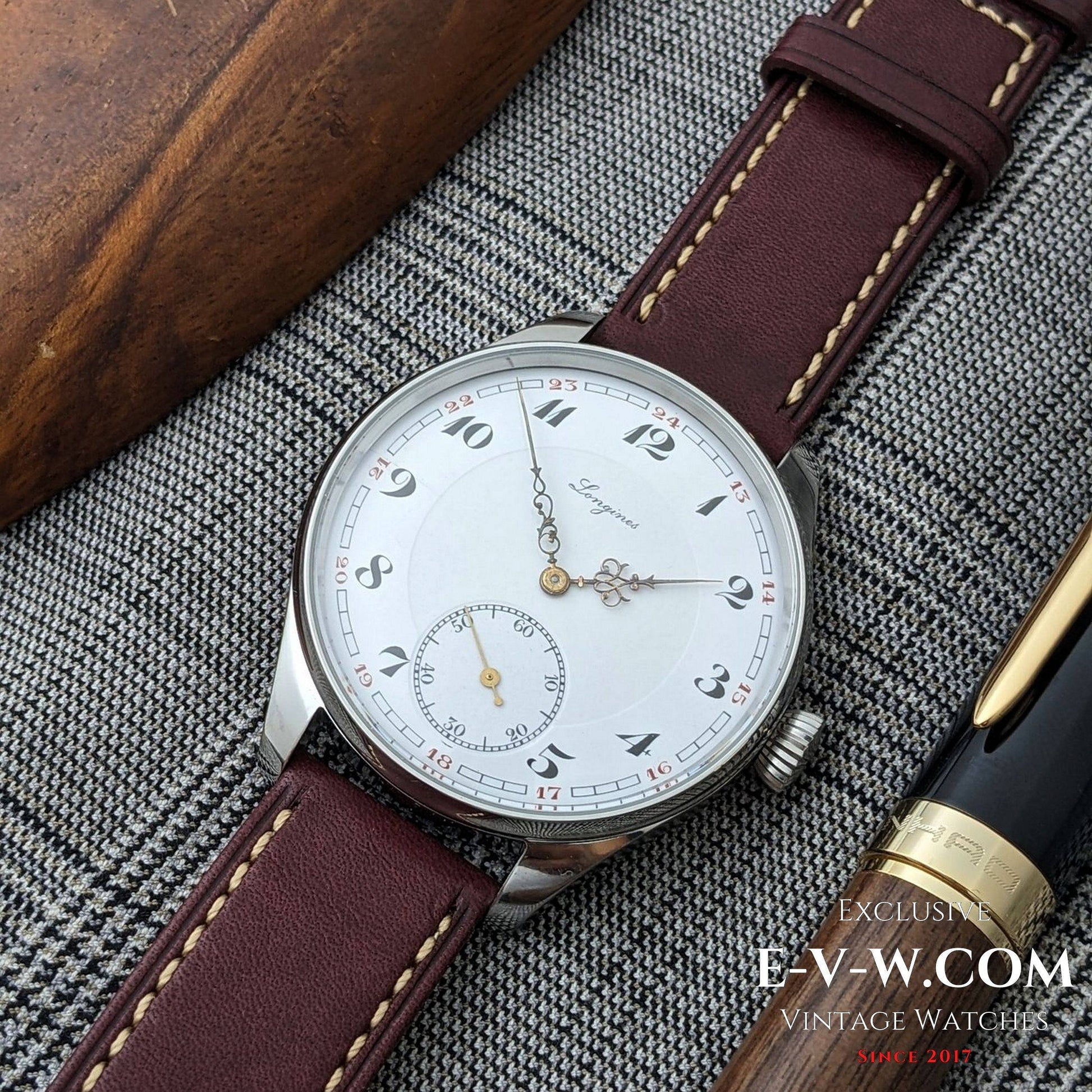 Vintage watch with brown leather strap on a textured surface, featuring E-V-W.COM branding.