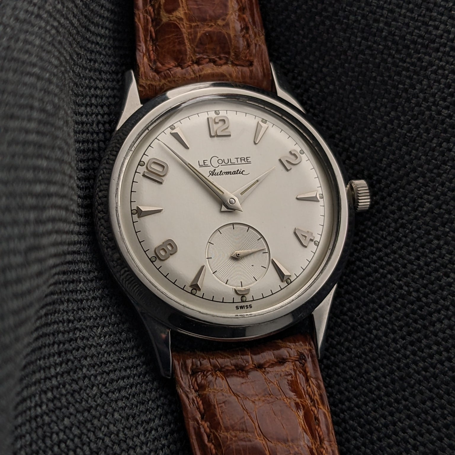 Front-facing Jaeger-LeCoultre Automatic E328 with a light dial, Arabic numerals, small seconds subdial, and brown textured strap.