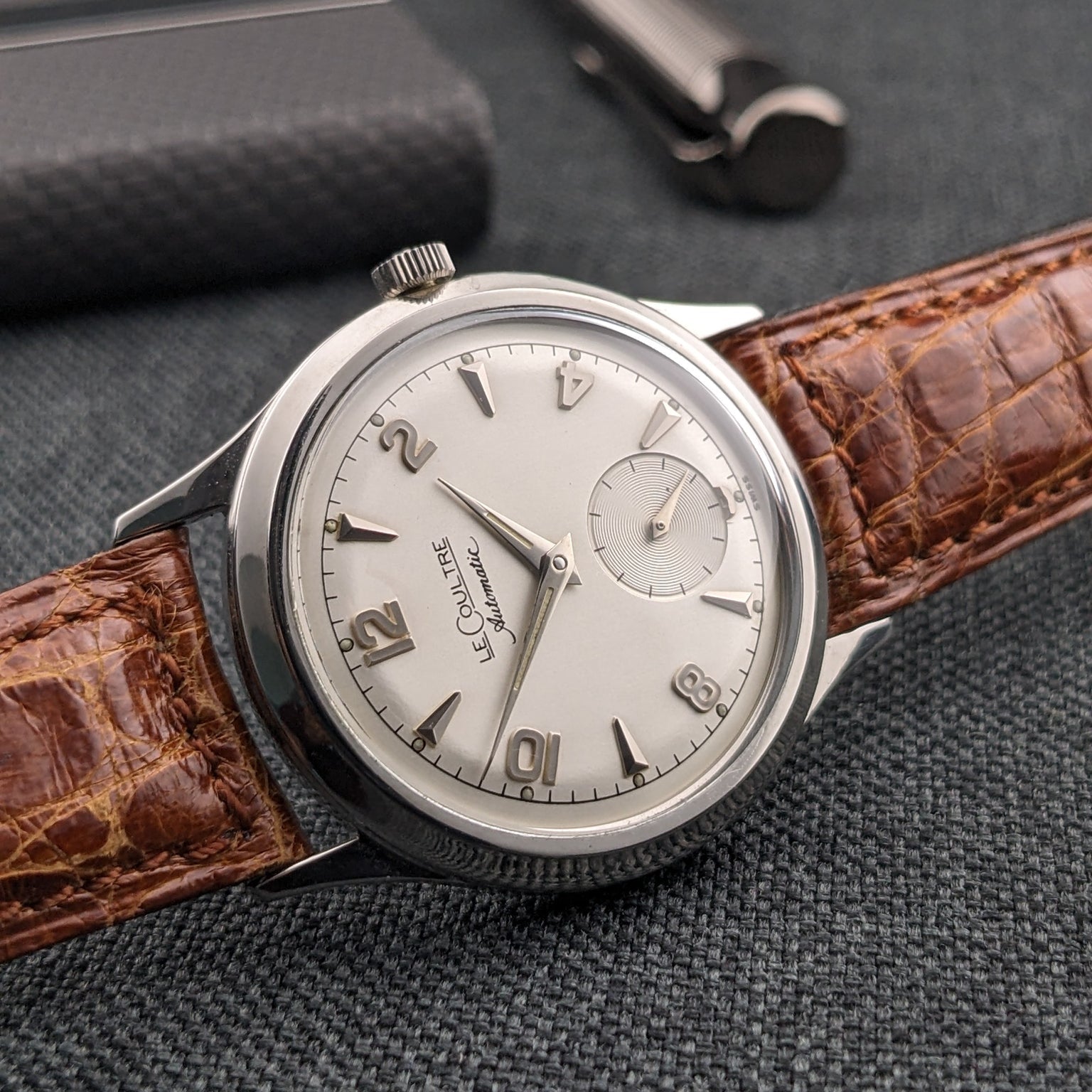 Angled Jaeger-LeCoultre Automatic E328 on a brown strap, with a silver-tone dial and pen in the background.