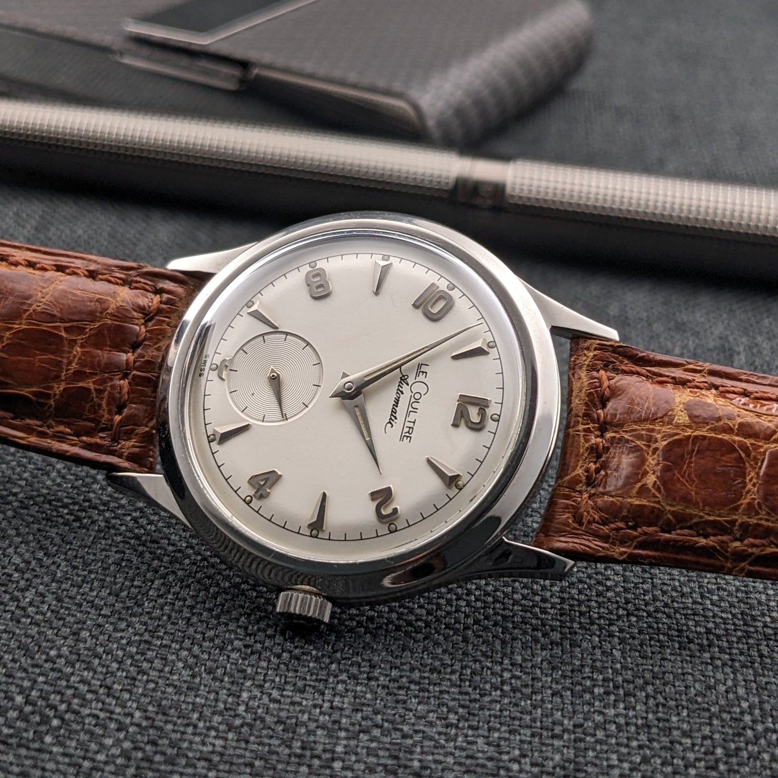 Jaeger-LeCoultre Automatic E328 lies horizontally with its dial visible, accompanied by a pen and black card holder.