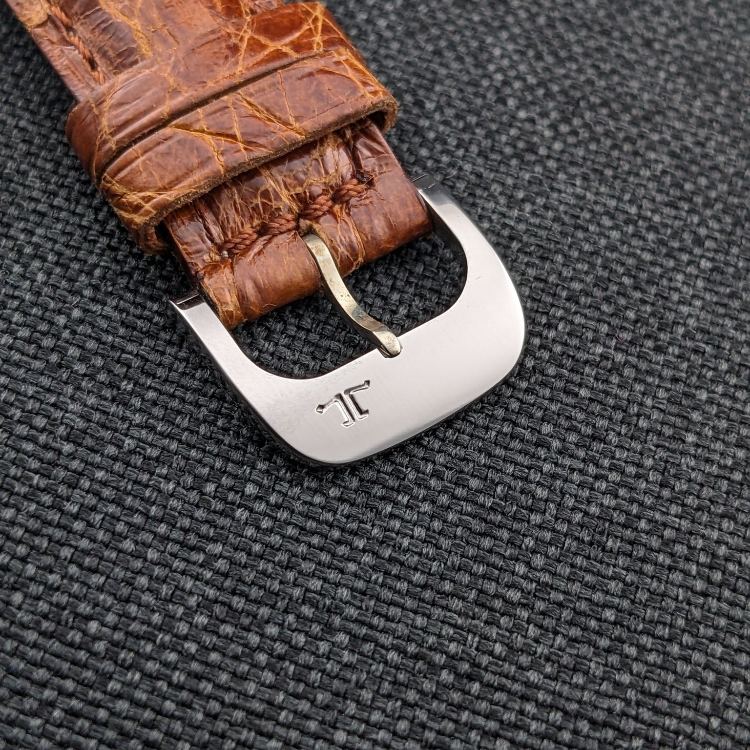 Close-up of the brown strap end and metal buckle on the Jaeger-LeCoultre Automatic E328, marked with a stylized emblem.