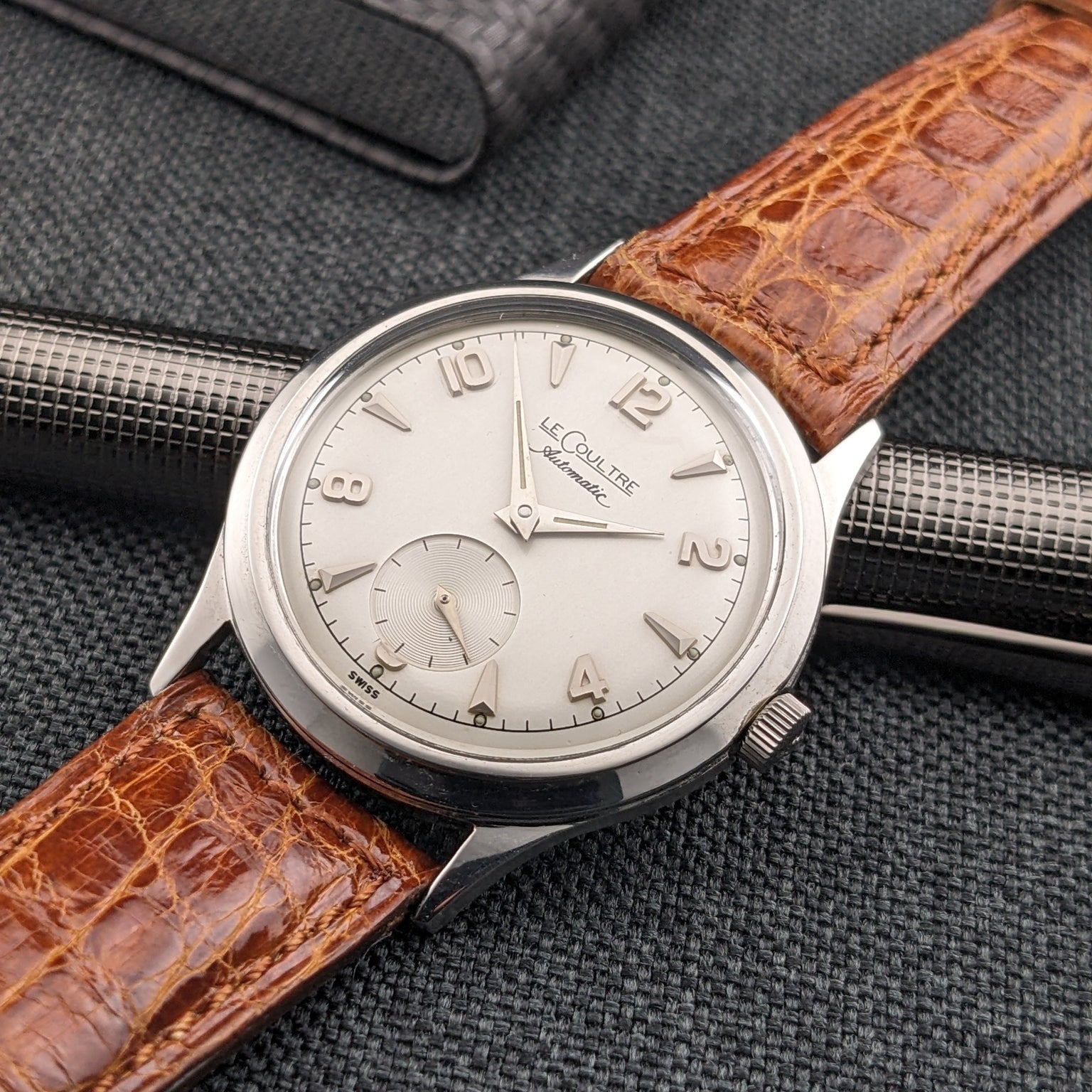 Jaeger-LeCoultre Automatic E328 shown at an angle over a textured pen, with its light dial and brown strap visible.